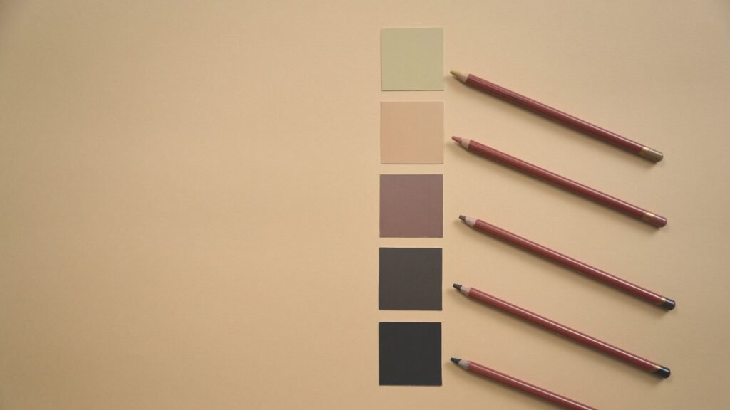 Flat lay of colored pencils and earthy tone swatches on a beige background, perfect for art and design contexts.