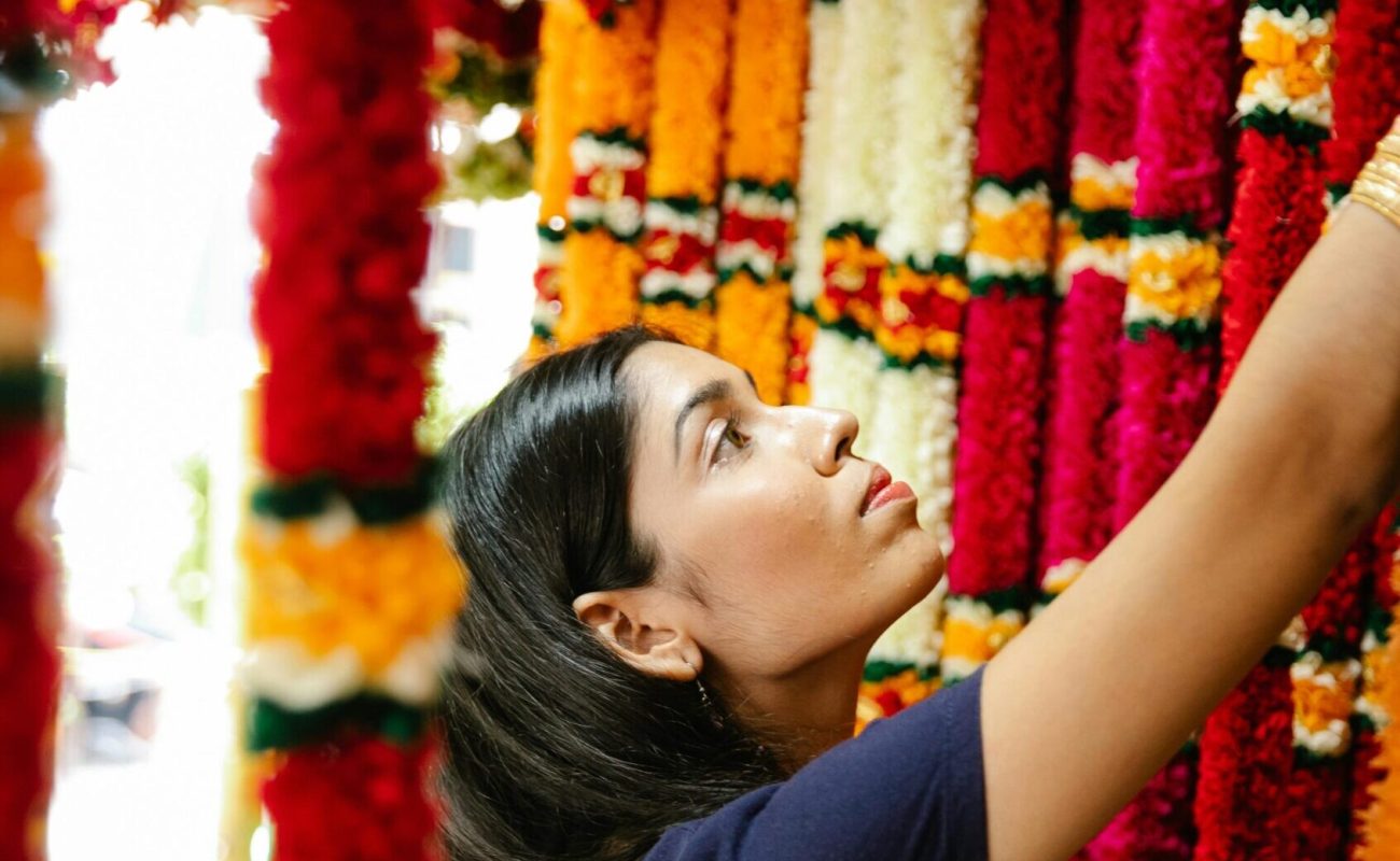 A woman selects colorful garlands at a vibrant traditional market.